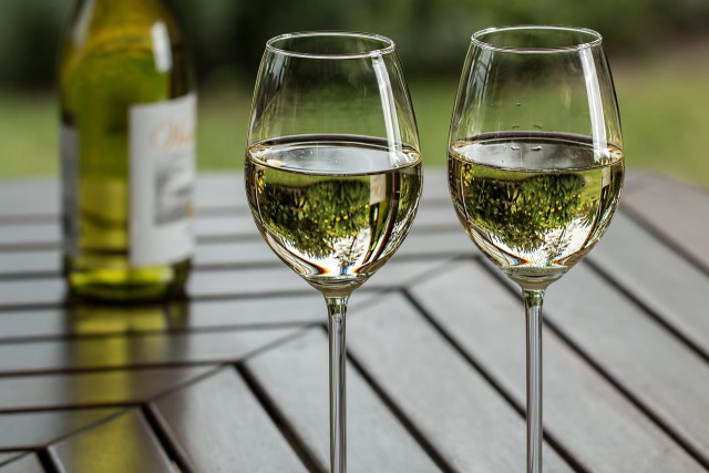 2 glasses of white on a table with a bottle in the background